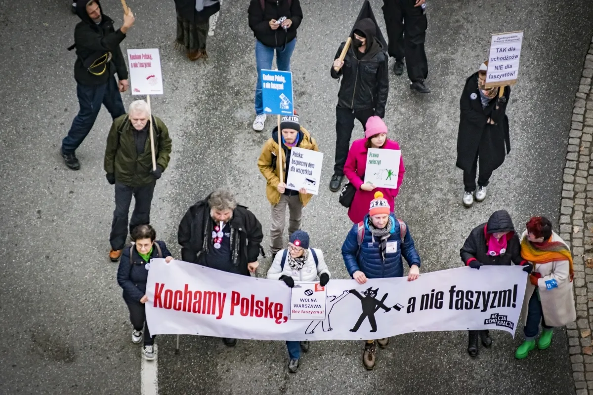 Overhead view of marchers carrying a long banner reading Kochamy Polske, a nie faszyzm!